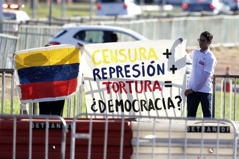 People hold a Venezuelan flag and sign that reads "Censorship, plus repression, plus torture, equals democracy?" outside Itamaraty palace where regional leaders are attending the South American Summit in Brasilia, Brazil, Tuesday, May 30, 2023. South America’s leaders are gathering as part of President Luiz Inácio Lula da Silva’s attempt to reinvigorate regional integration efforts. (AP Photo/Gustavo Moreno)