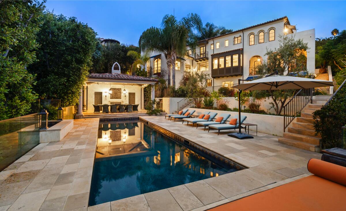 A rectangular pool next to a small house and, up some steps, a three-story home.