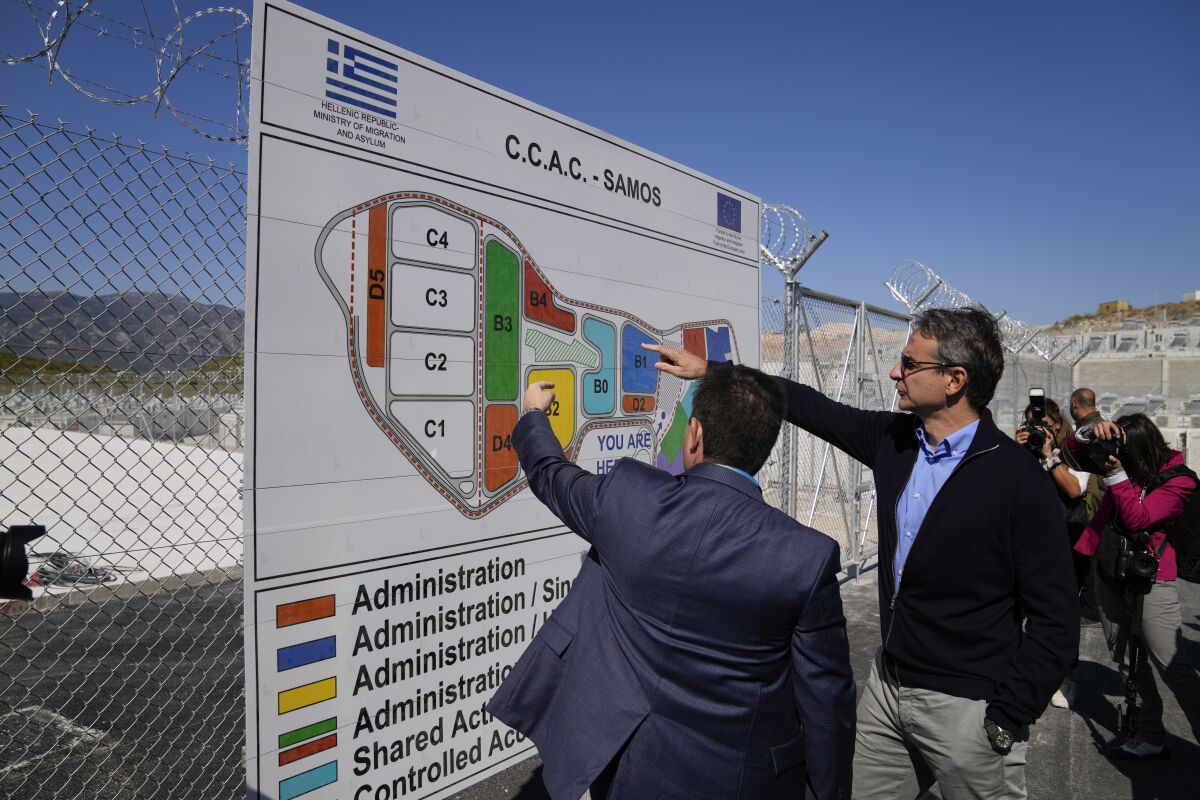 Greece's Prime Minister Kyriakos Mitsotakis,second left, looks at a billboard during his visit at the new closed monitored facility for migrants and refugees in Zervou village, on the eastern Aegean island of Samos, Greece, Friday, Oct. 1, 2021. Greek authorities have moved ten days ago asylum-seekers living in a squalid camp on the island of Samos into a new facility on the island, where access are more strictly controlled. (AP Photo/Thanassis Stavrakis)