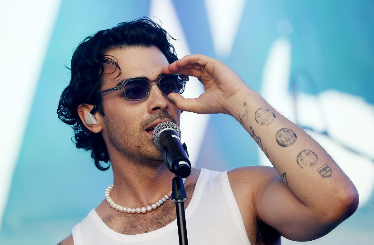 Joe Jonas performing in a white tank, pearl necklace and sunglasses. 