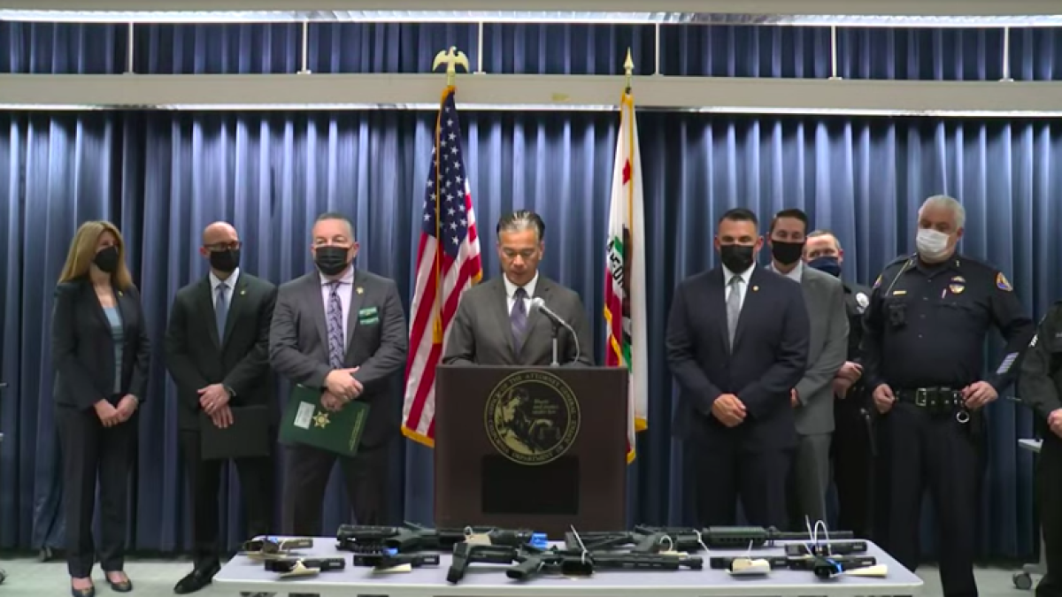 Law enforcement authorities stand near a table full of weapons.