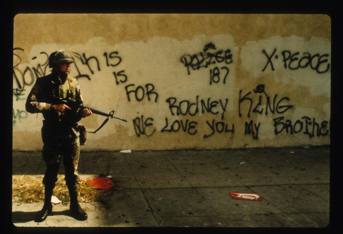 A National Guardsman stands near graffiti that spells out support for Rodney King on April 30, 1992.