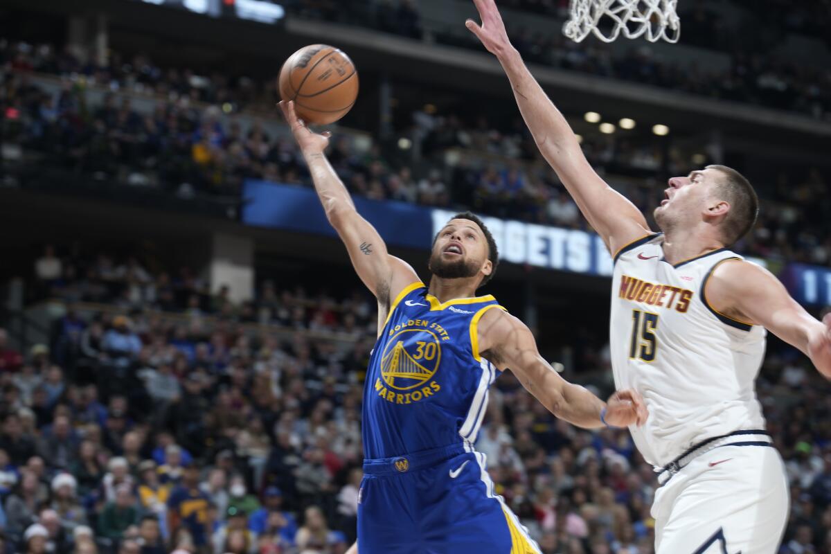 Warriors guard Stephen Curry, left, drives to the rim as Nuggets center Nikola Jokic looks to block the shot in Denver.