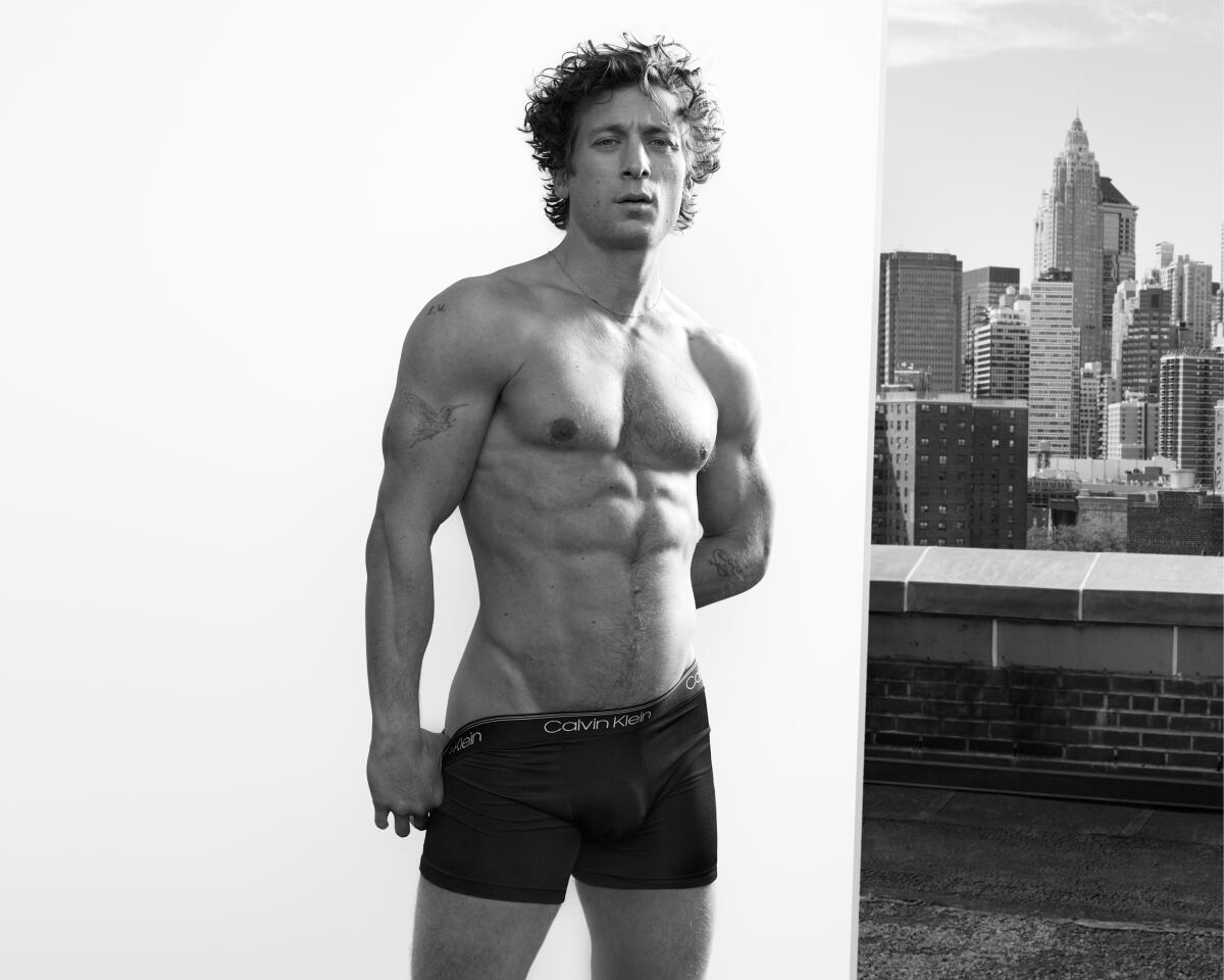Jeremy Allen White stands on a New York City rooftop in his underwear with skyscrapers behind him.