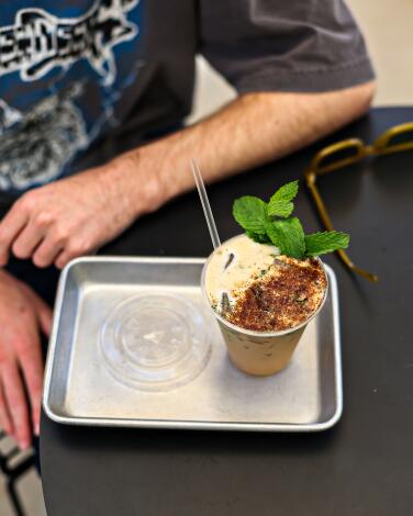A metal tray holds a coffee drink with a mint garnish