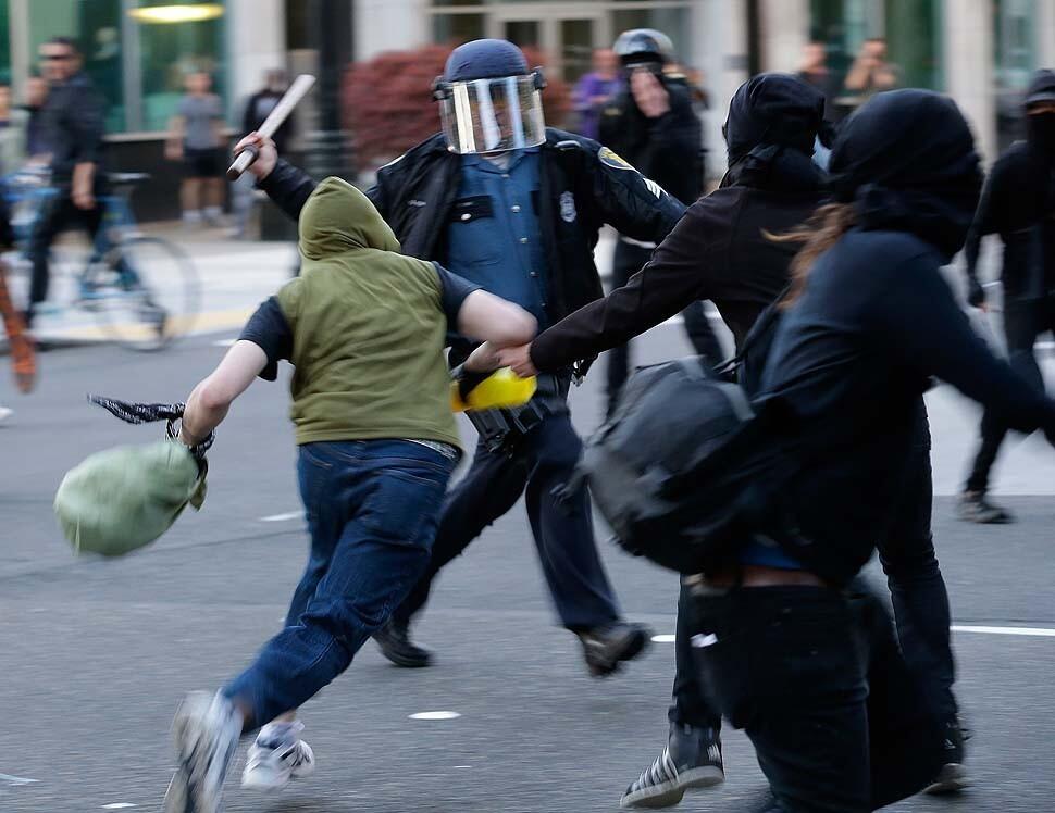 A police officer swings a baton at protesters as an "anti-capitalism" May Day march in Seattle on Wednesday devolved into clashes between demonstrators and police.
