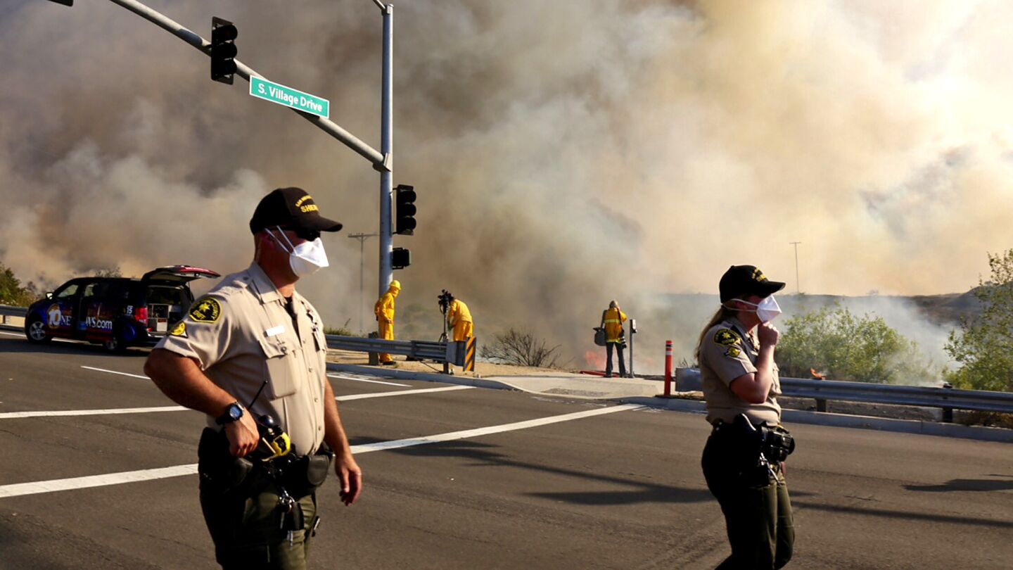 San Diego County sheriff's deputies monitor traffic in San Marcos as a wildfire burns along the hillsides on Wednesday. Multiple fires across Southern California damaged or destroyed more than a dozen homes.