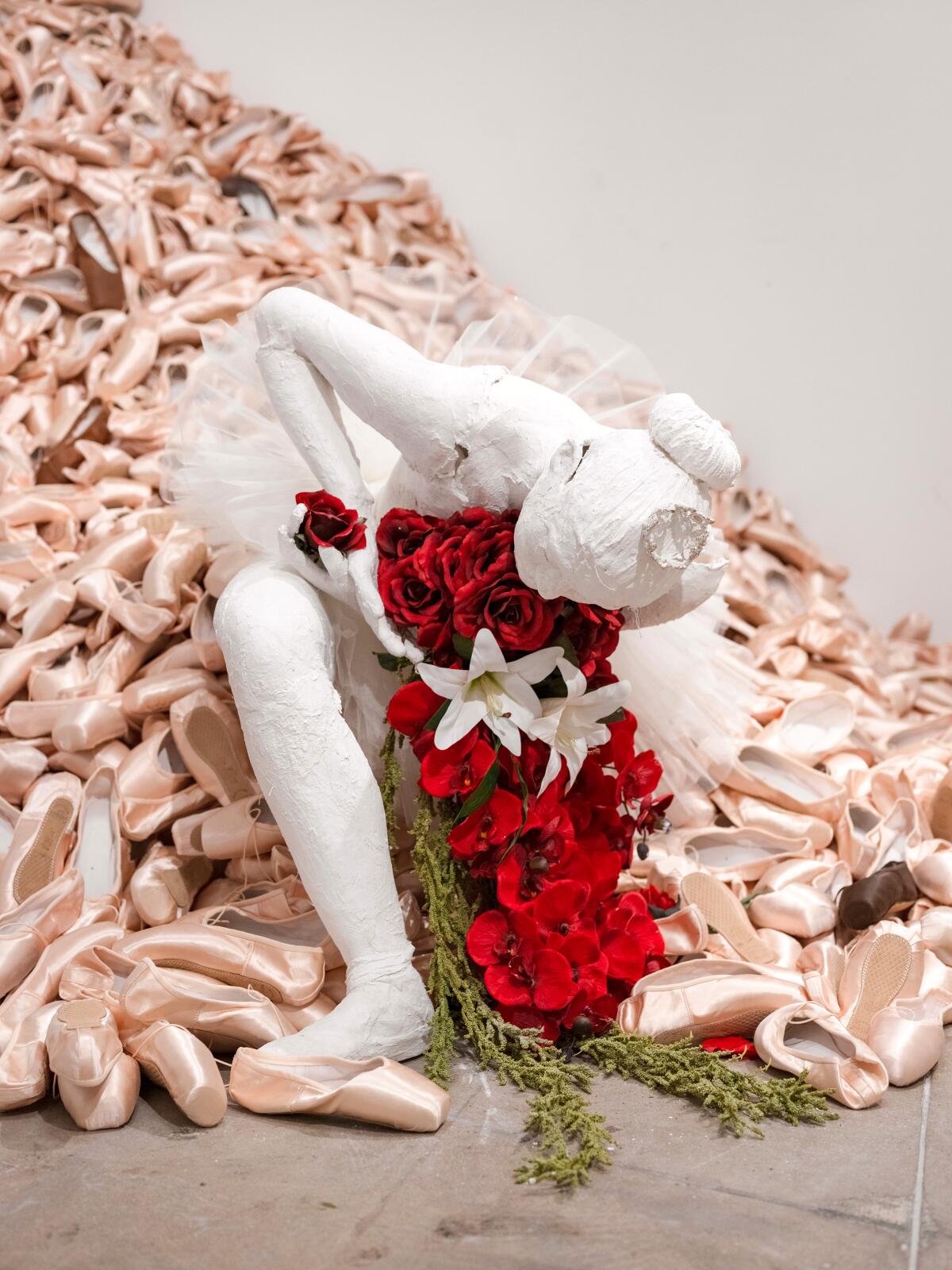 A sculpture of a ballerina sitting on a pile of pink pointe shoes.