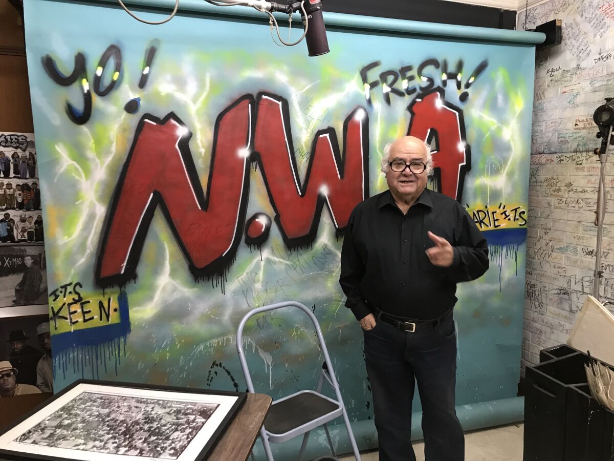 Photographer George Rodriguez in his downtown Los Angeles studio in April 2018. Behind him is a backdrop he employed for an early shoot with N.W.A.
