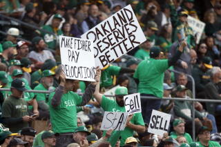 People in green T-shirts holding signs that say "Sell" and "Oakland Deserves Better"