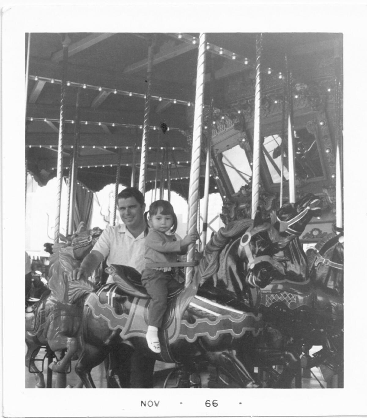 A black and white photograph of a father and daughter on a merry-go-round.