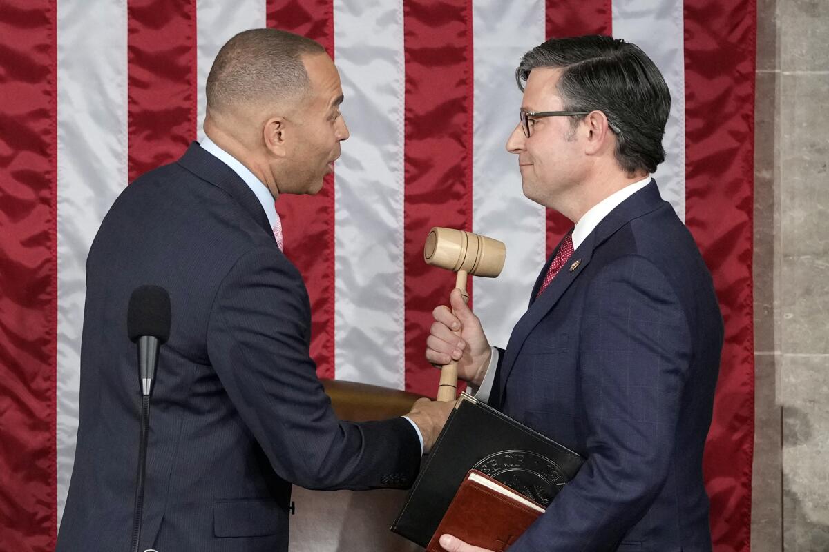 House Minority Leader Hakeem Jeffries speaking to Rep. Mike Johnson and handing him a gavel in front of a large American flag