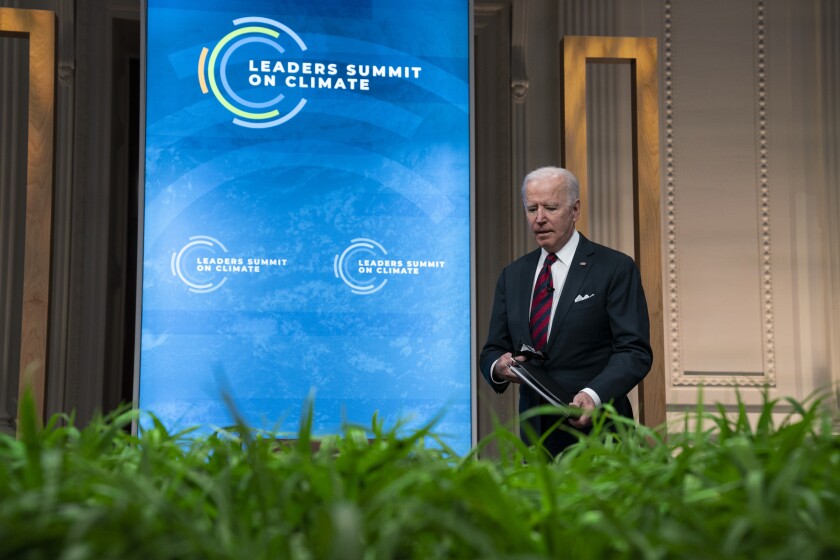 President Biden stands next to a blue screen.