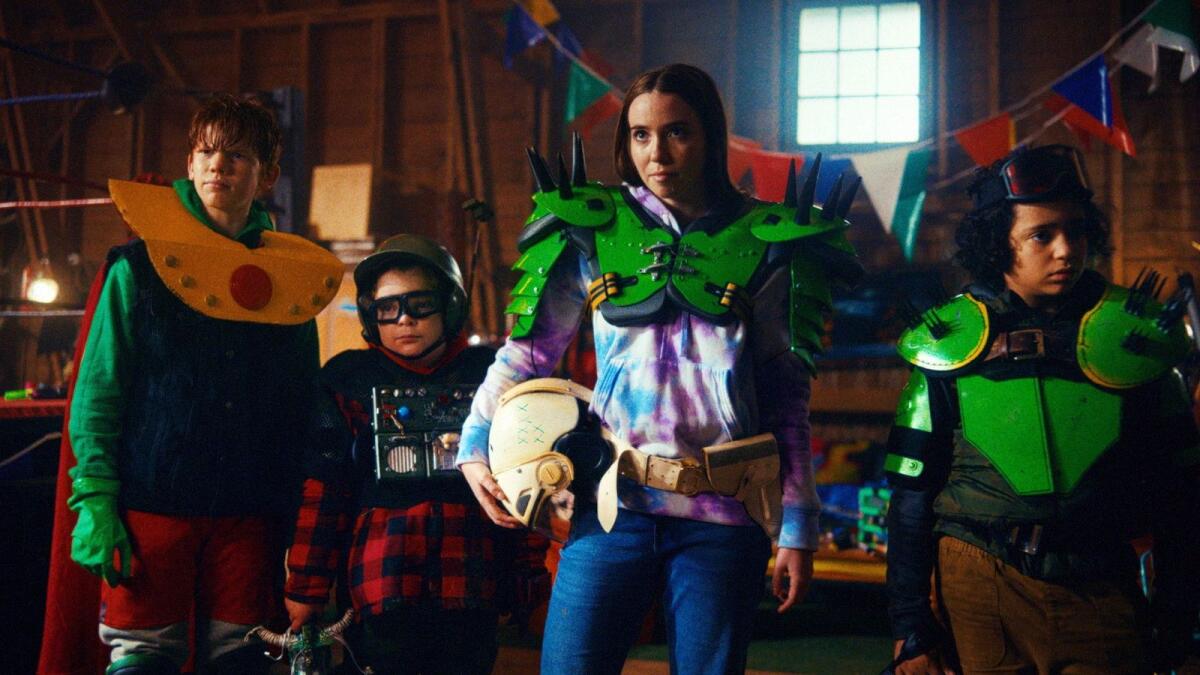 Four kids wearing colorful armor and helmets stand in a living room