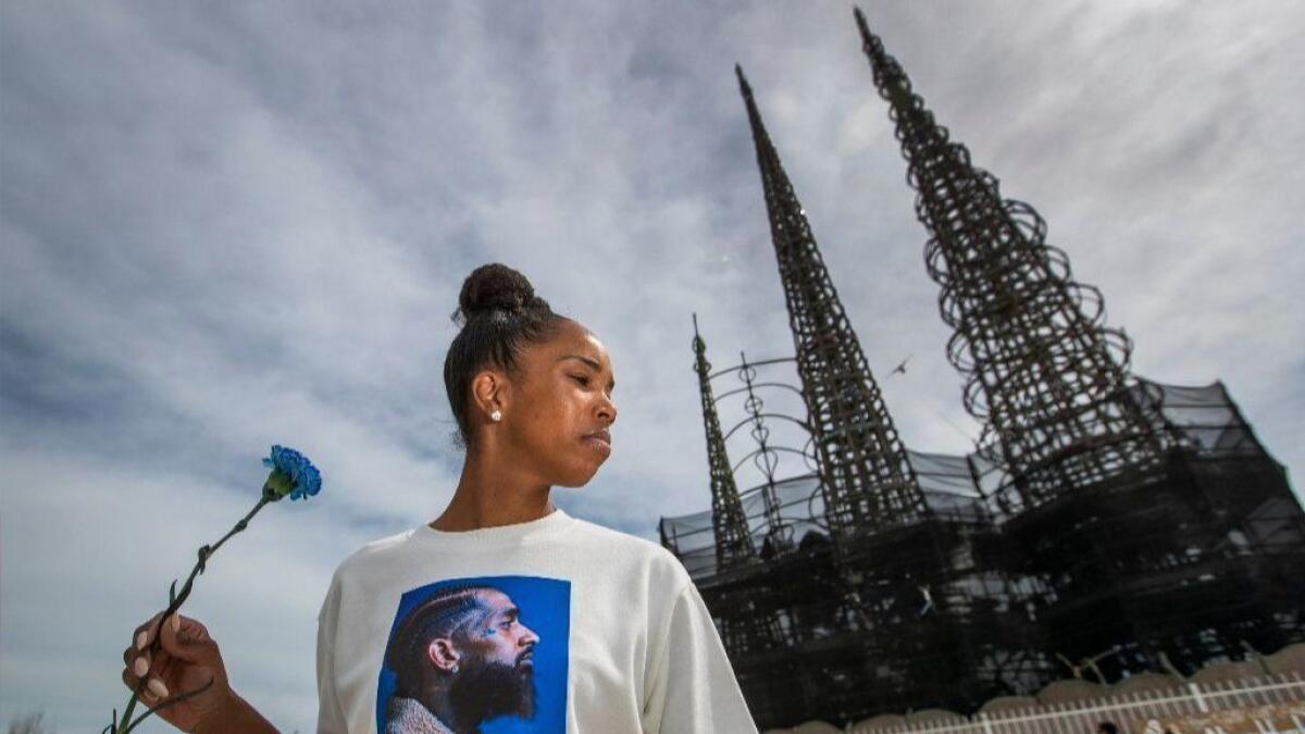Ladeisha Williams of Watts holds a flower and wears a Nipsey Hussle shirt as community members gathered Thursday near the Watts Towers to watch the slain rapper's funeral procession.