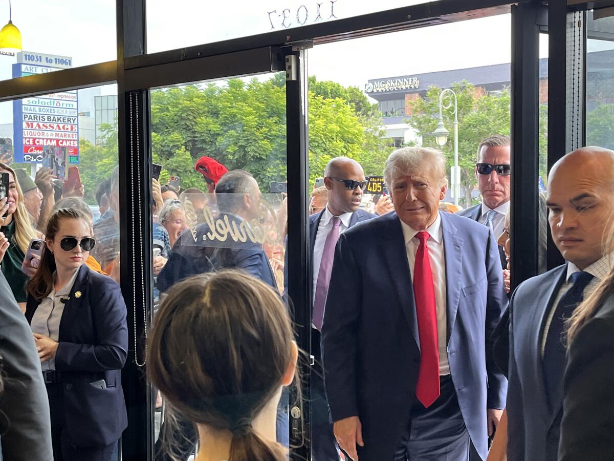 Donald Trump walks through a door surrounded by many people. 