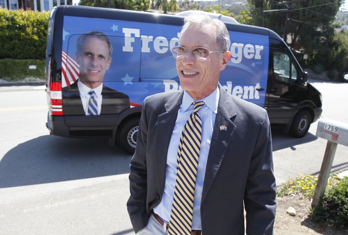 A man in a suit and tie stands in front of a van emblazoned with a presidential campaign ad bearing his image 
