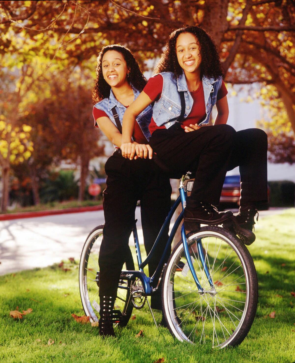 Identical twins on a bicycle in the series "Sister, Sister"