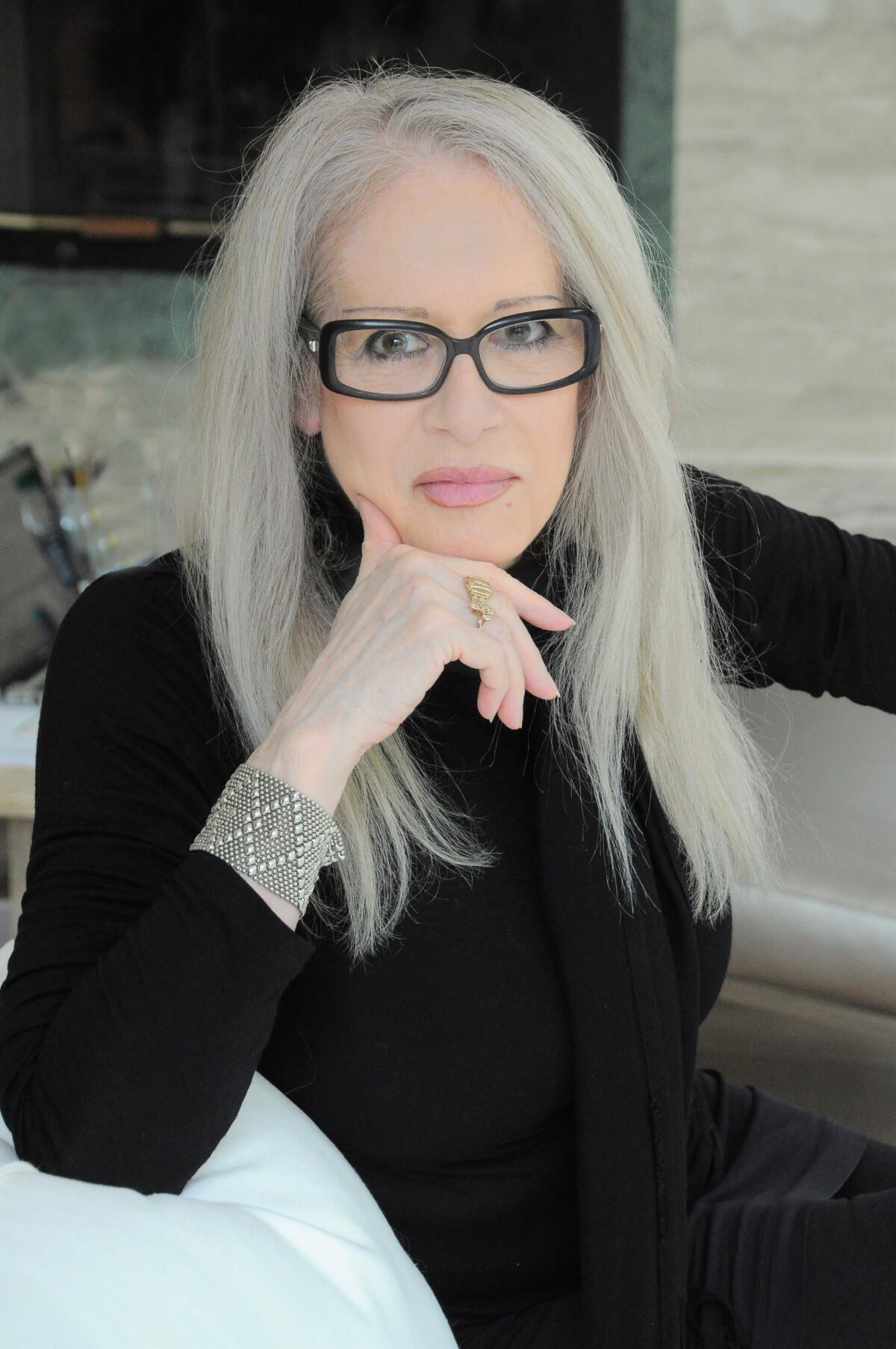 A woman with long white hair and dark-rimmed glasses