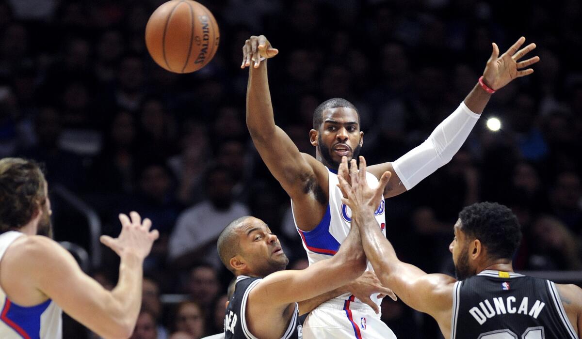 Clippers point guard Chris Paul leaps to make a pass to teammate Spencer Hawes over Spurs point guard Tony Parker and forward Tim Duncan in the first half.