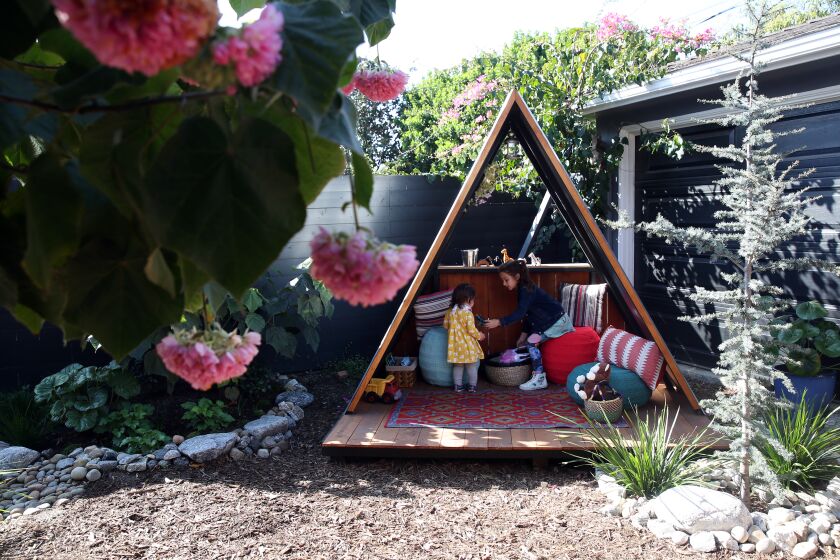 LONG BEACH, CALIFORNIA-FEBRUARY 16, 2020: Talia and Nili Glatstein, left and right, play in the A-Frame playhouse in the backyard of their house on February 16 , 2020, in Long Beach, California. The pink flowers on the left are Dombeya Wallichii also known as a Pink Ball Tree. (Photo By Dania Maxwell / Los Angeles Times)
