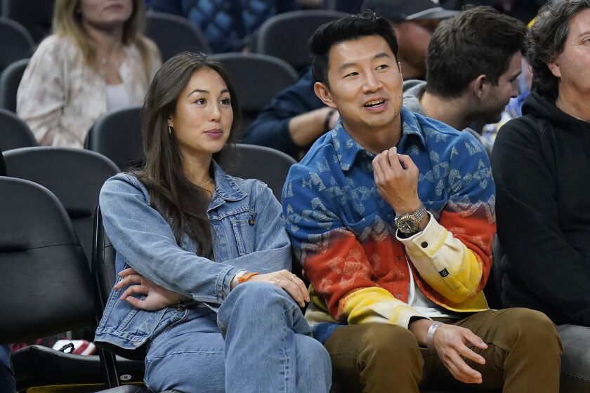 FILE - Actor Simu Liu, right, watches an NBA basketball game between the Golden State Warriors and the Miami Heat in San Francisco, Oct. 27, 2022. Marvel Shang-Chi actor Liu wants everyone who attends an event at Chase Center to feel welcome, comfortable and supported, just as he has been in the five months since opening up about his own challenges with anxiety. (AP Photo/Jeff Chiu, File)