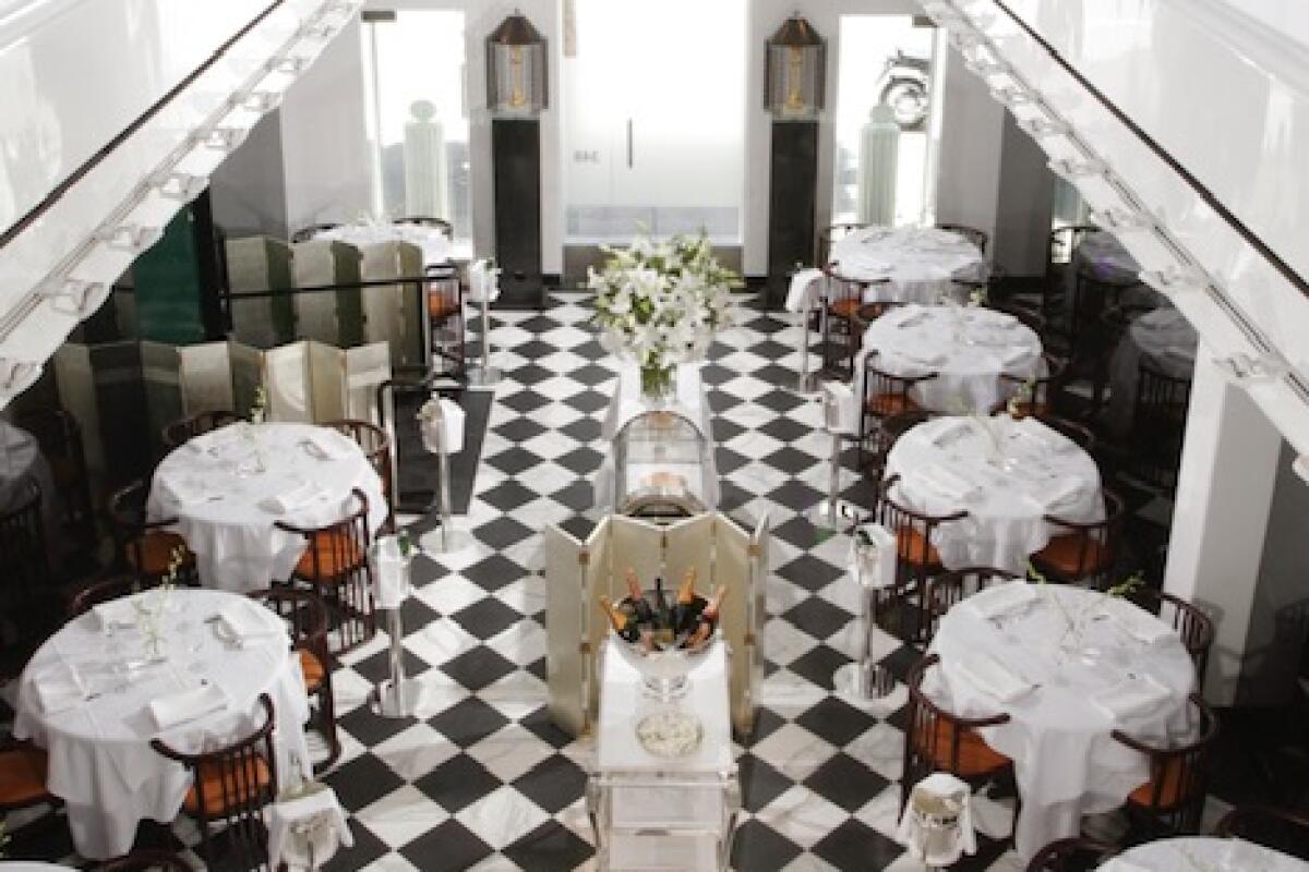 A view from above of a restaurant dining room with a checkerboard floor and white-clothed tables.