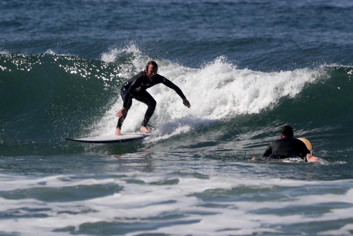 A surfer stands up on his board riding a wave as another surfer floats nearby.