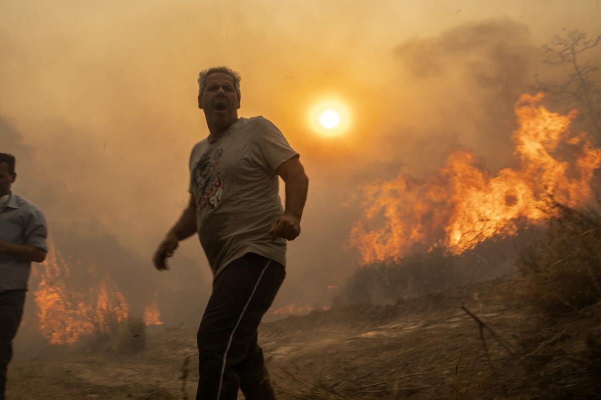 A man reacts as flames burn trees on the Aegean Sea island of Rhodes, Greece.