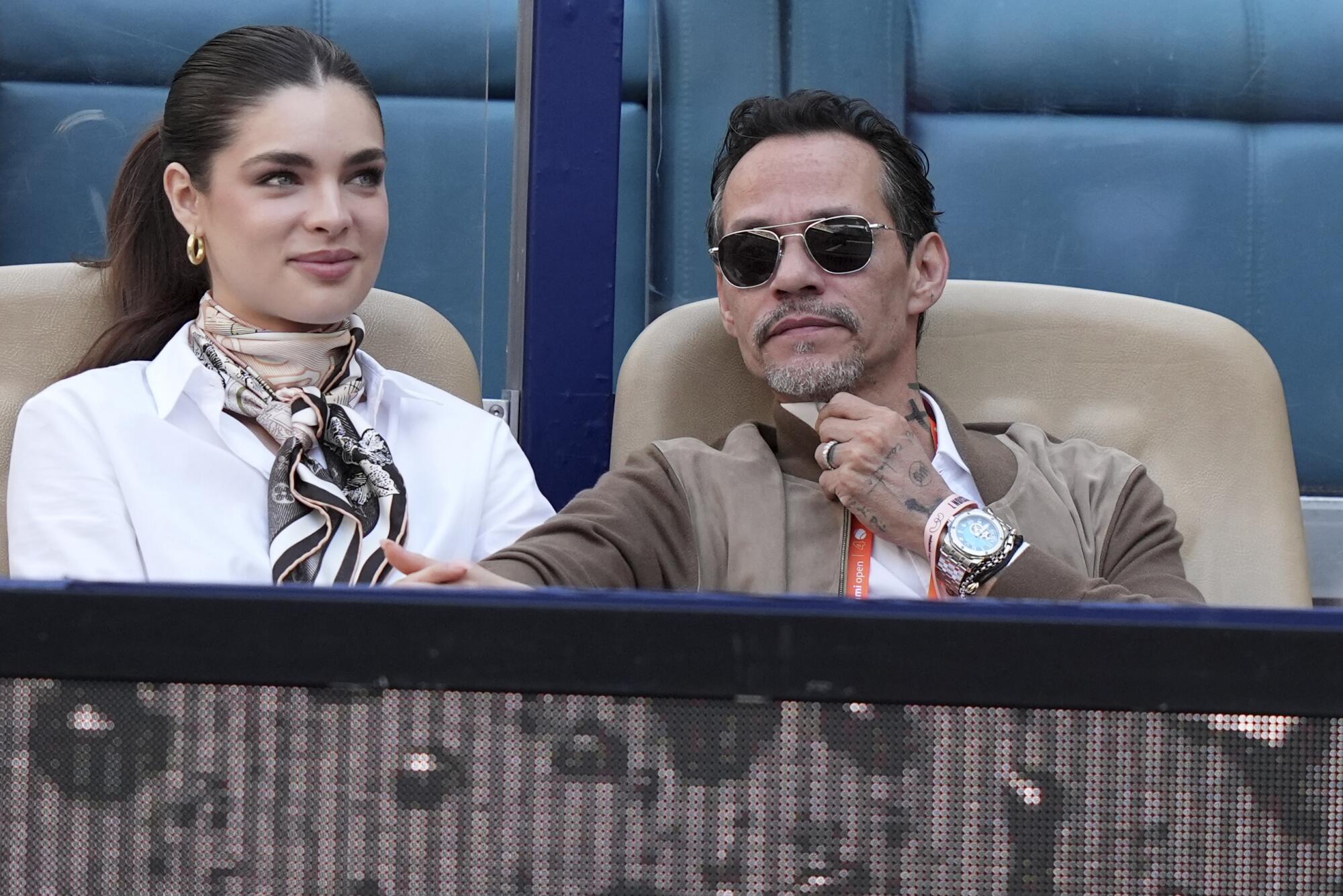 Marc Anthony, a la derecha, se sienta en la cancha con su esposa Nadia Ferreira