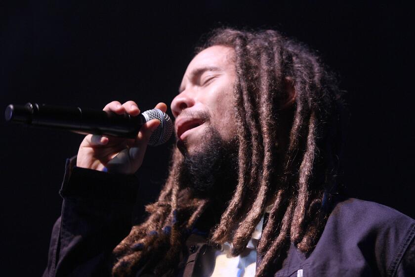 A man with long brown dreadlocks singing into a microphone with his eyes closed