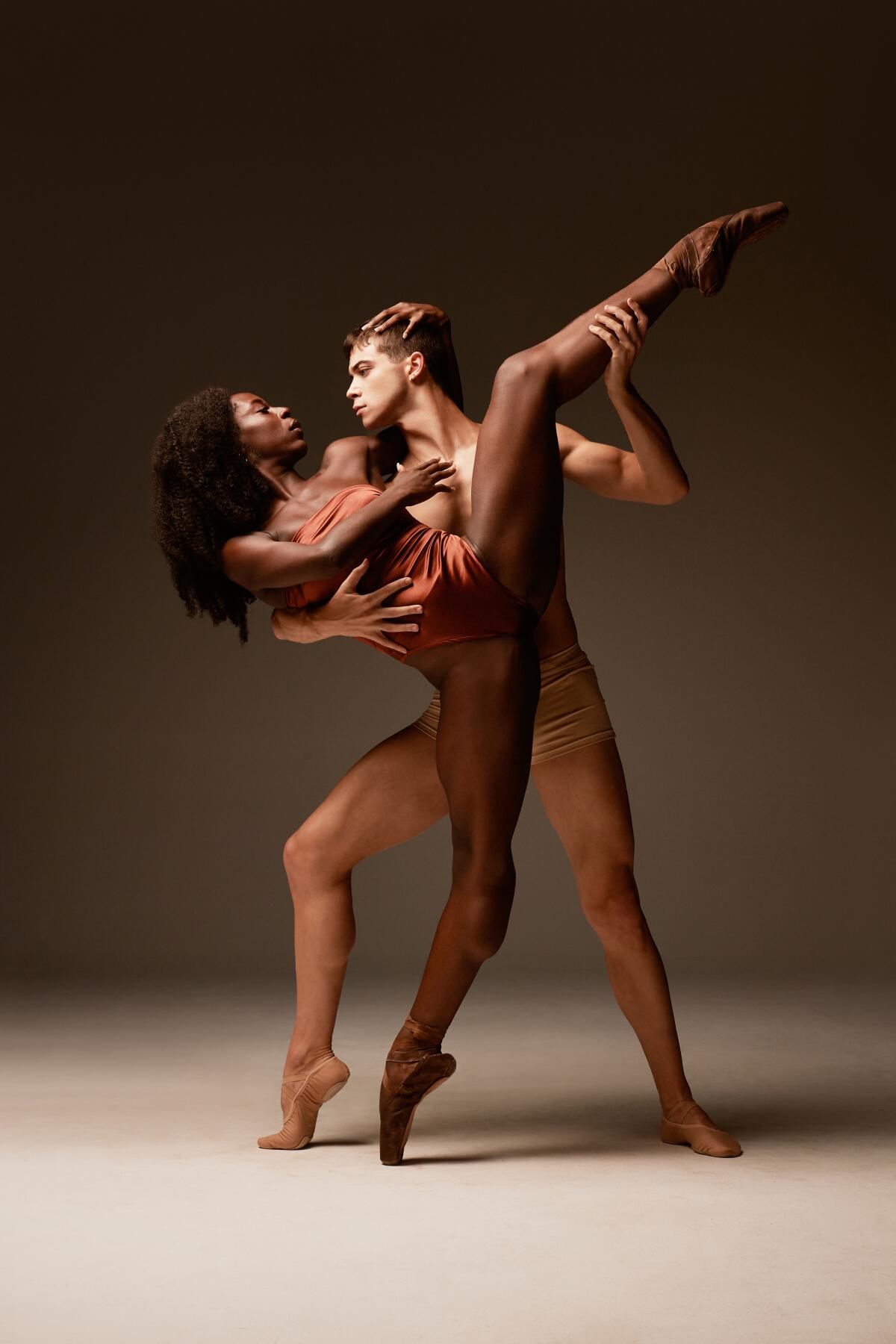 A male dancer holds up the extended leg of a female dancer.