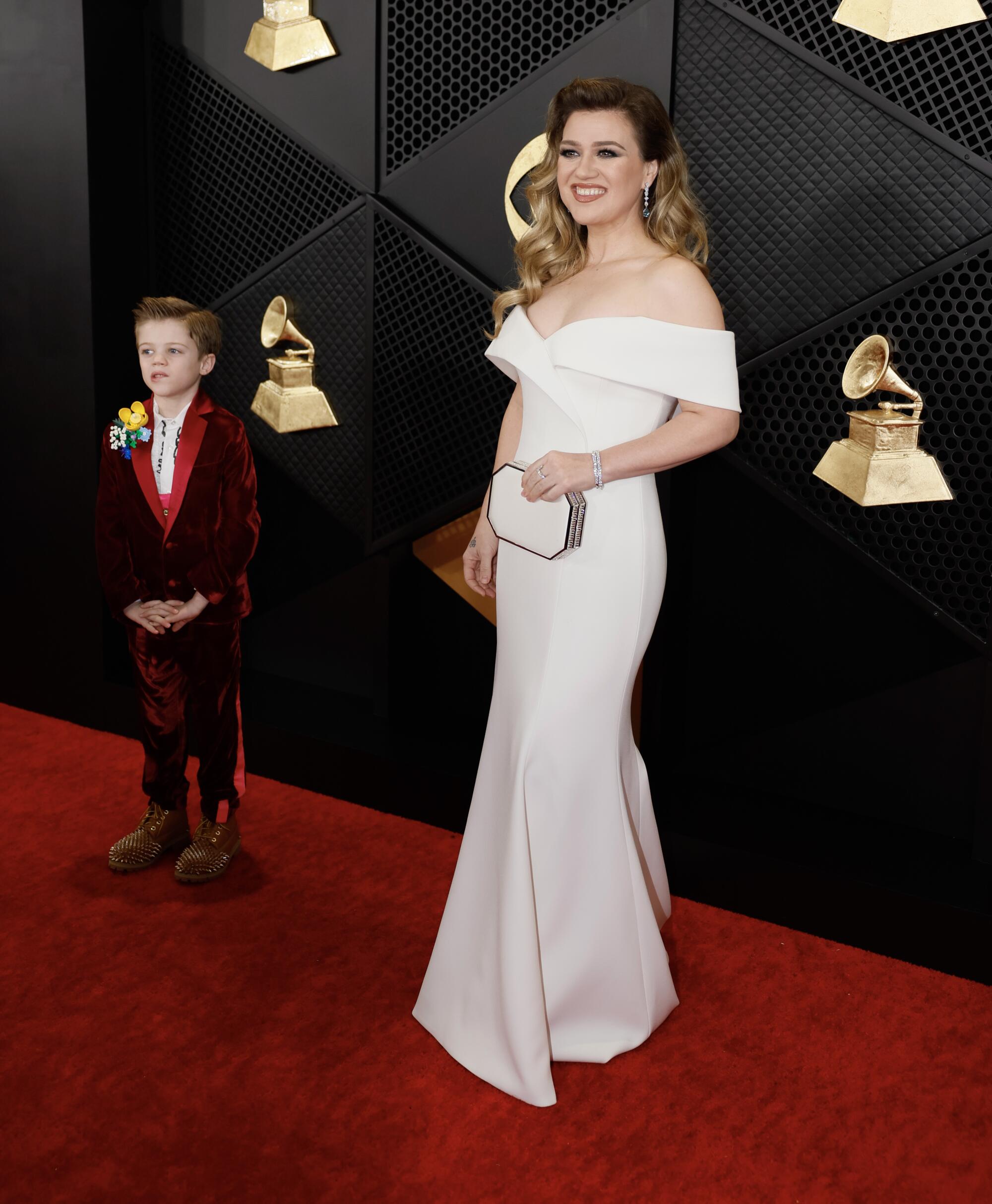 Kelly Clarkson wears a white dress as she poses with her young son, who wears a dark red velvet suit 