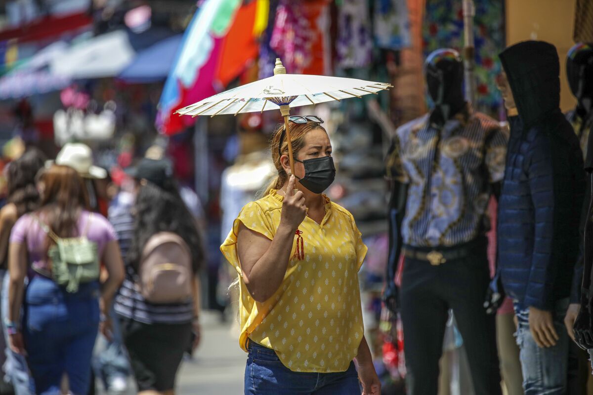 A woman in a yellow shirt and jeans wears a face mask and holds an umbrella.