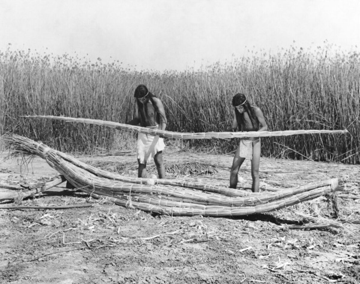 A pair of Native American men construct a boat, called a balsa, using tule bulrushes in California, in the late 1920s or early 1930s.