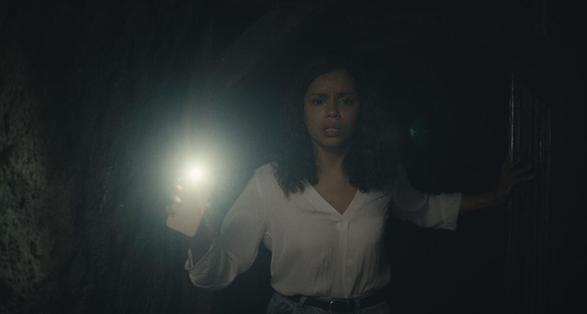 A young woman uses the flashlight on her cellphone to illuminate a dark area