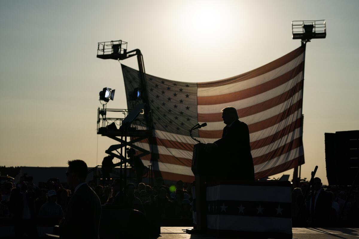 President Trump is silhouetted in front of a U.S. flag as the sun shines through