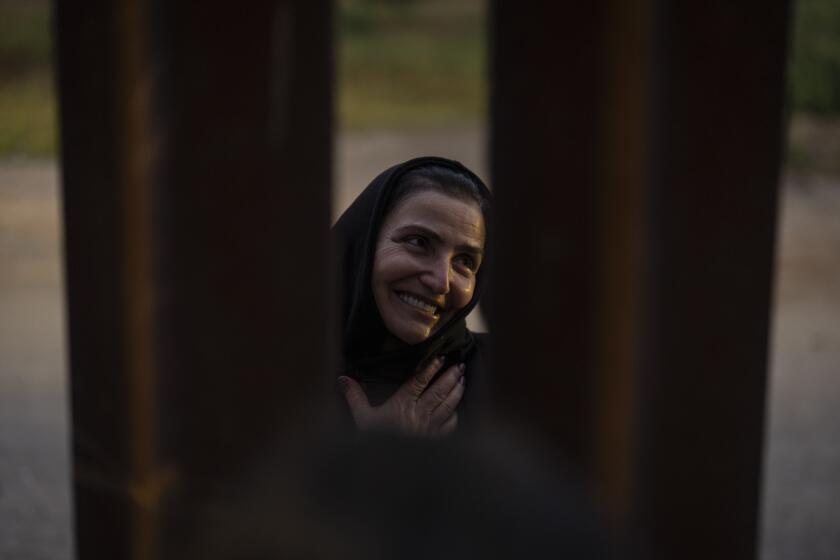 Georgian migrant Nani, smiles as she thanks a U.S. volunteer, speaking between gaps in one of the border walls separating Tijuana, Mexico, and San Diego, as she waits to apply for asylum with U.S. authorities, Friday, April 12, 2024, seen from San Diego. (AP Photo/Gregory Bull)