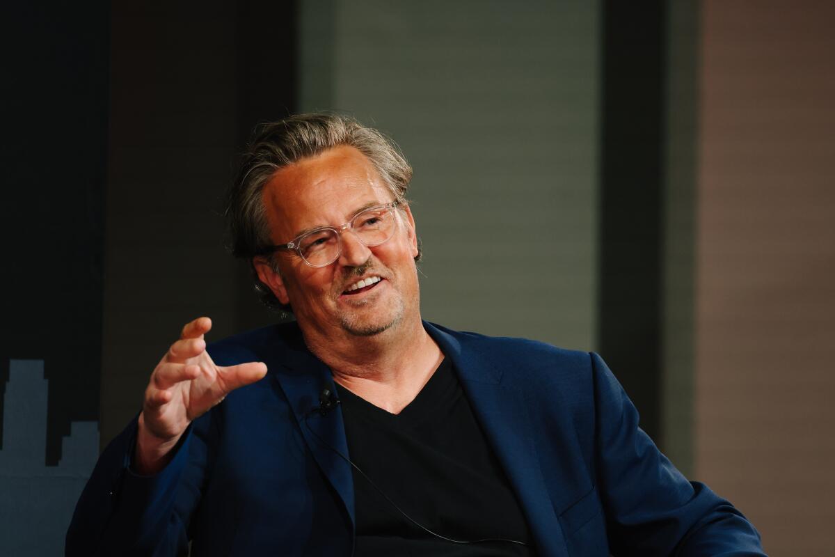 Matthew Perry smiles while speaking and gesturing with his hand.