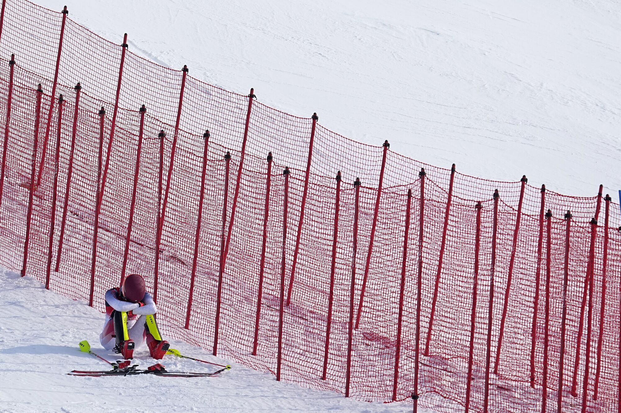 Mikaela Shiffrin sits in the snow next to the ski course with her head buried in her arms.