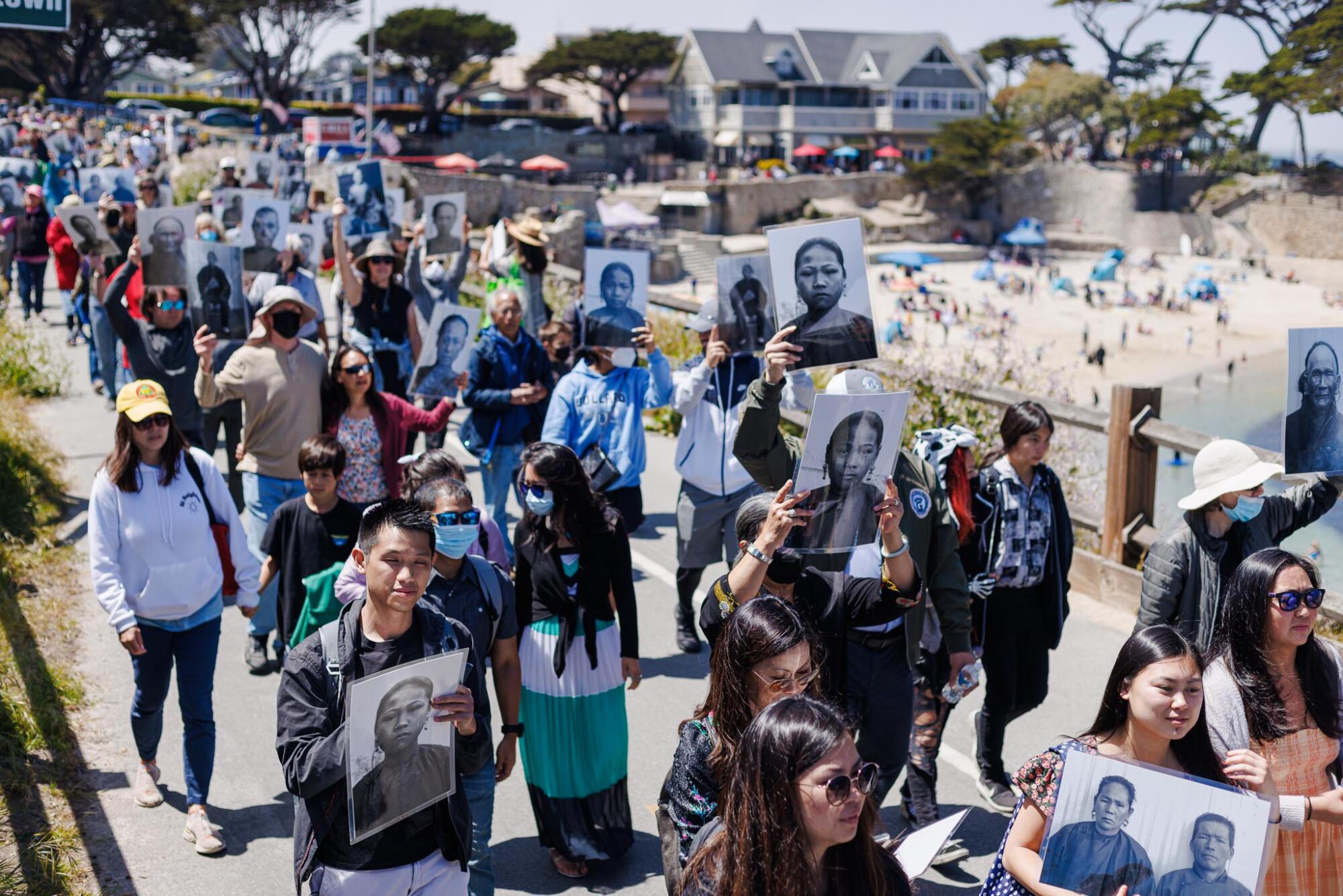 A crowd marching with enlarged historic portraits of people of Asian descent.
