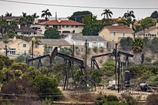 Homes overlook a field of oil pumpjacks.