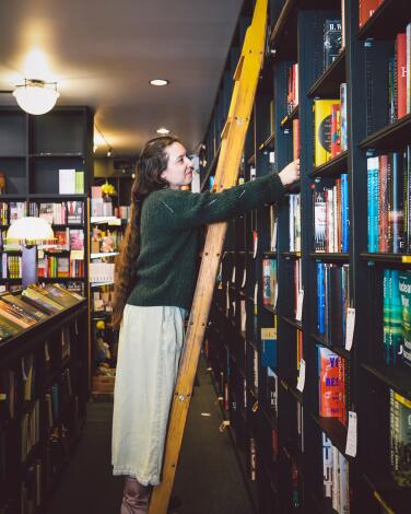 A person on a yellow ladder that's leaning against full black bookshelves