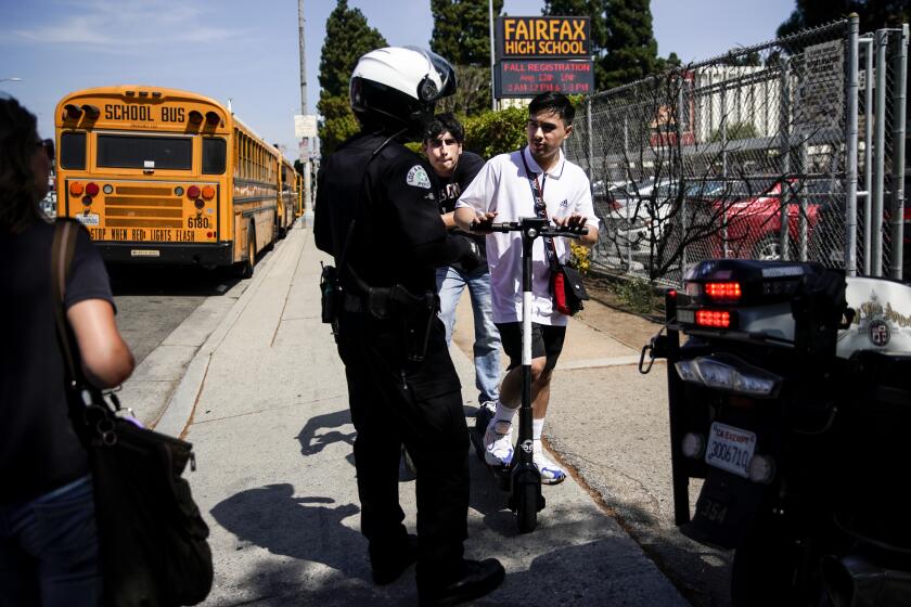 LOS ANGELES, CALIF. - AUGUST 22: An LAPD bike officer warns two young men about riding their e-scooters on the sidewalk, in front of Fairfax High School near the intersection of North Fairfax Avenue and Melrose Avenue on Thursday, Aug. 22, 2019 in Los Angeles, Calif. (Kent Nishimura / Los Angeles Times)