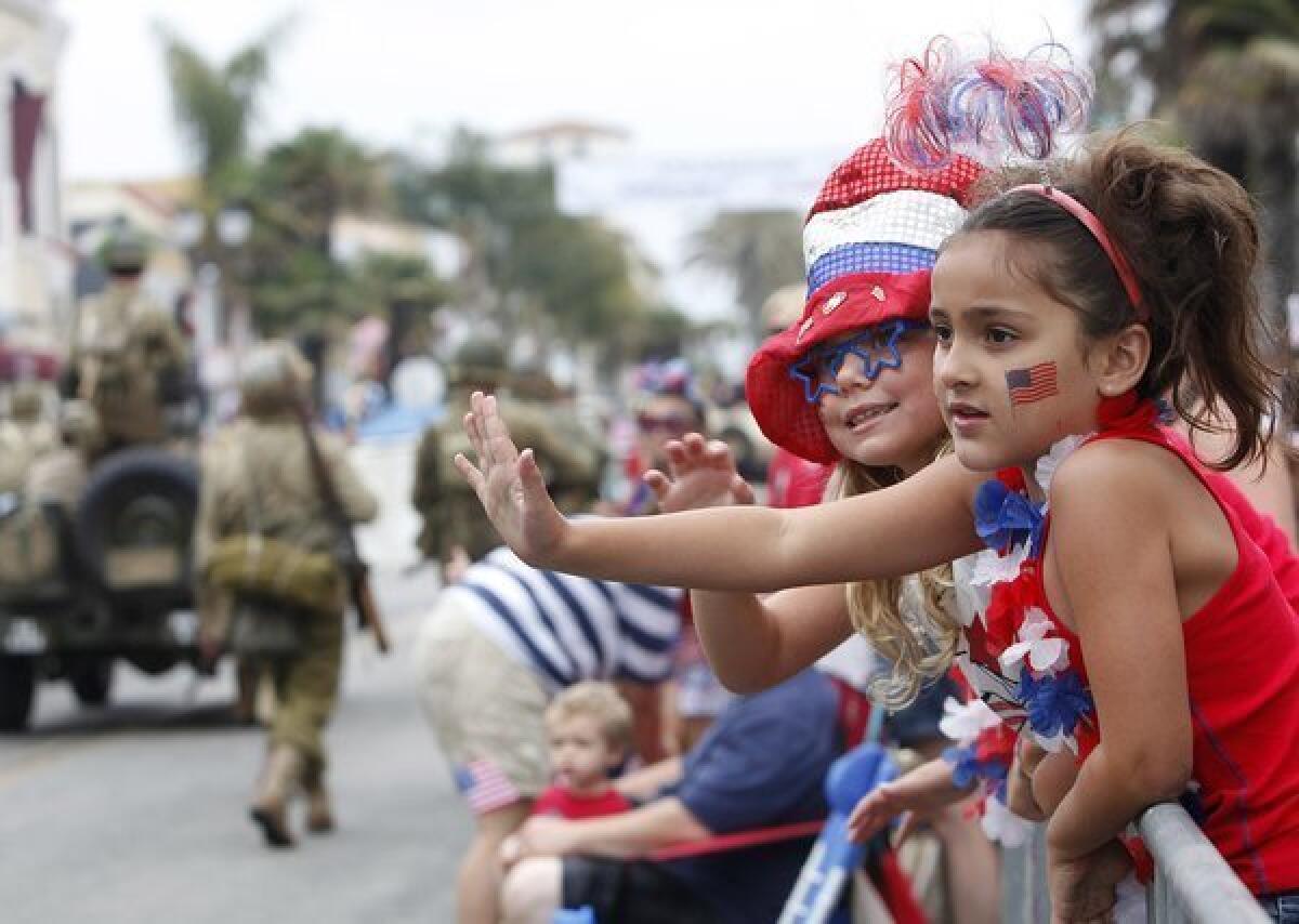 Brooklynn Peters, 6, right, and Sandahl Blake, 7, second from right, wave as they watch the Huntington Beach Independence Day Parade last year.