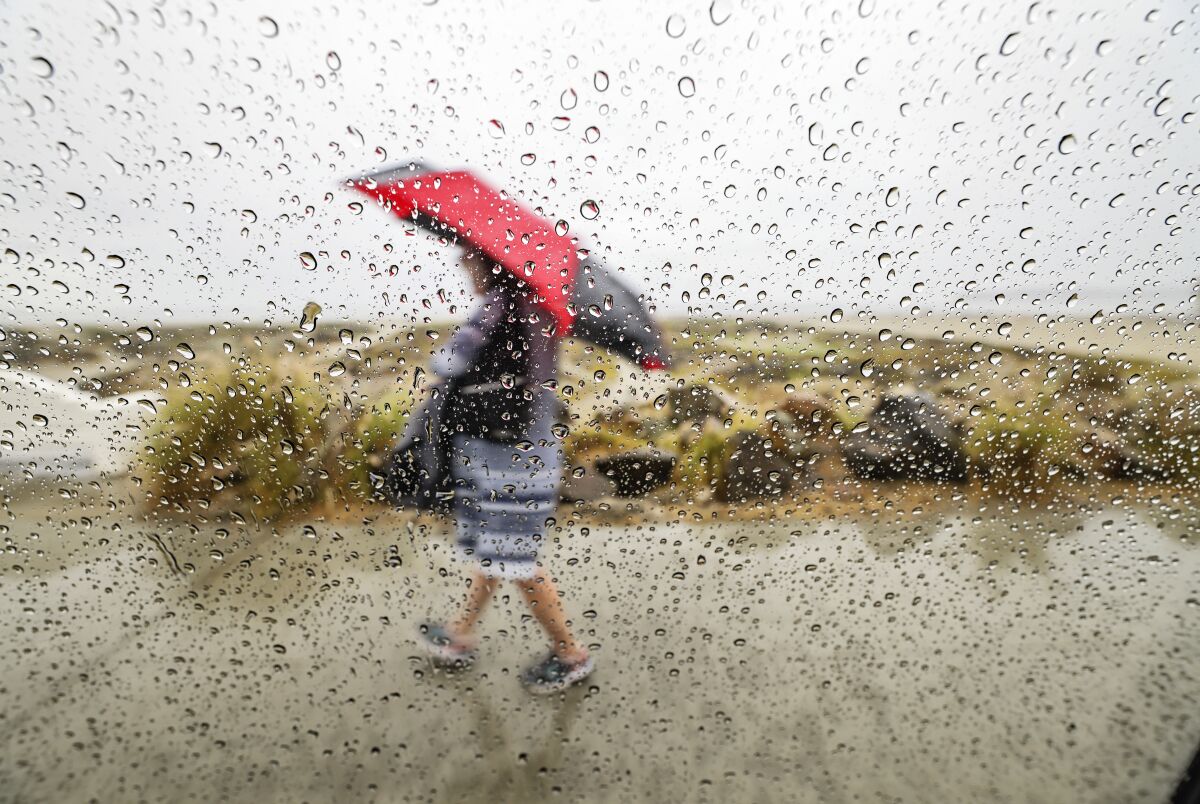 Despite wind and rain, a person walks by the beach along Ocean Boulevard on Friday in Coronado.