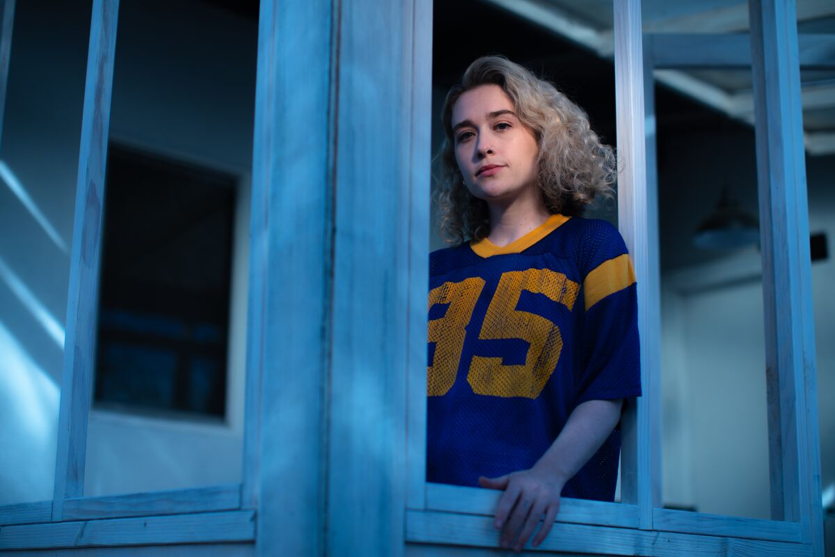 A woman in a football jersey looks out from behind a window sill