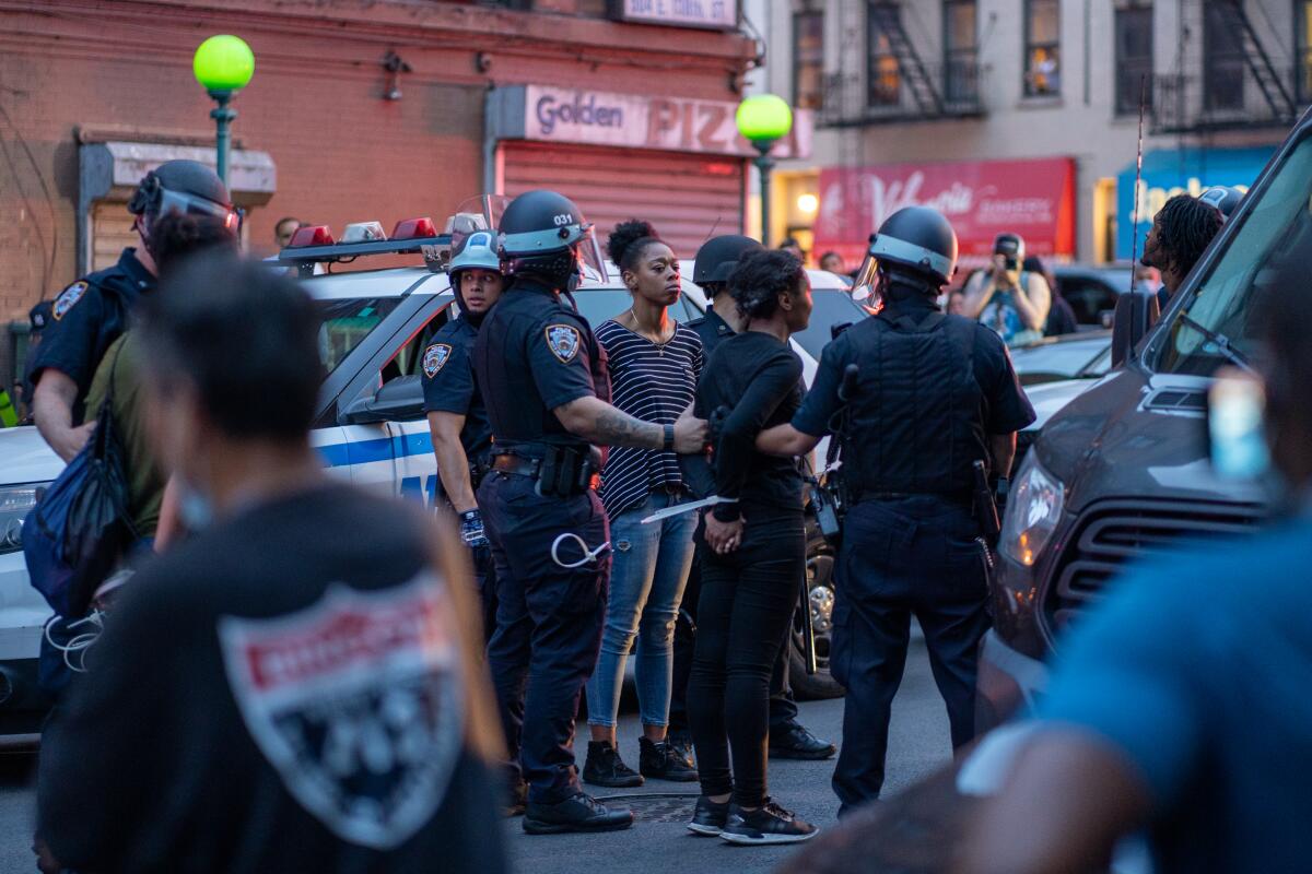 Police officers hold onto handcuffed protesters in a city street