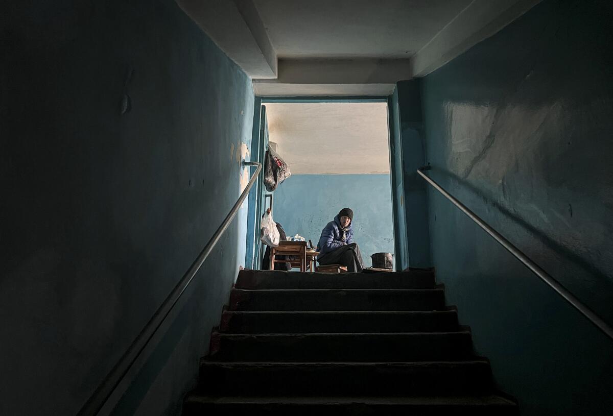 Looking up a dark staircase, with a person in coat and hat sitting at the top