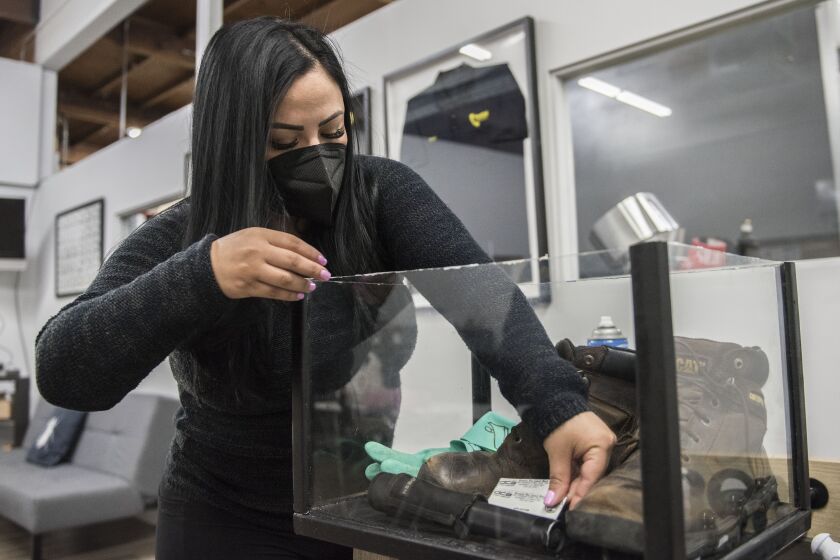 Nidia Campos of Pestcal Exterminators, places her brother Sergio Ayala's work gear in a display case at the company's office in North Hollywood on Friday, Feb. 26, 2021. Ayala died of COVID-19 on Jan. 3, 2021. ( Nick Agro / For The Times )